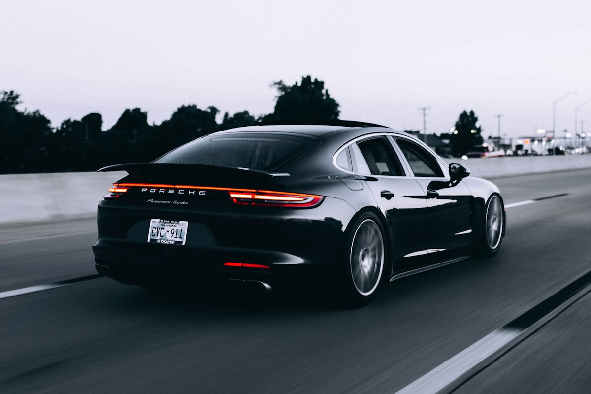 Dark sports car parked on an open road beneath a cloudy sky
